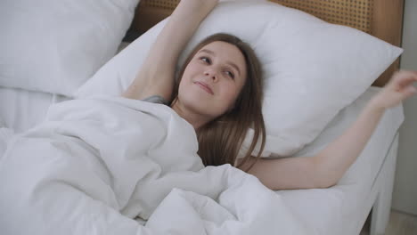 Woman-wakes-up-raise-stretches-hands-in-bed-feels-healthy